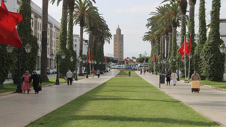 La photo montre la magnifique avenue Mohammed V, dans le centre-ville de Rabat, bordée de palmiers et d'espaces verts, avec en arrière-plan le minaret caractéristique de la mosquée Assounna.