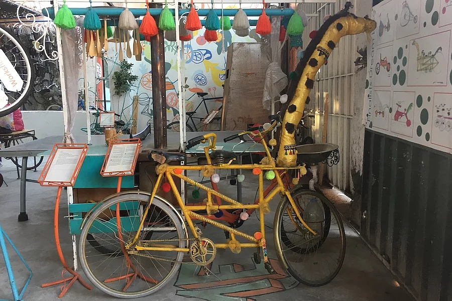 L'image montre une installation artistique saisissante en forme de girafe, située dans les locaux de l'initiative de vélos solidaires Pikala Bikes, au Maroc.